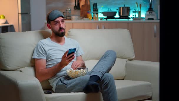 Hombre aburrido sentado en el sofá sosteniendo palomitas de maíz - Imágenes, Vídeo