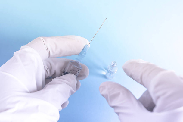 Flasche mit Impfstoff und Spritze in der Hand eines Forschers mit Handschuhen. Fläschchen mit Coronavirus-Impfstoff zum Schutz gegen COVID-19 entwickelt. Gesundheitswesen und medizinisches Konzept. Blauer Hintergrund - Foto, Bild