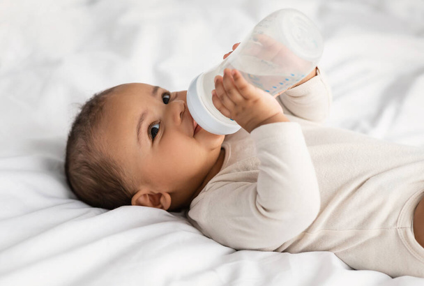 Cute little African American baby drinking water from bottle - Photo, Image