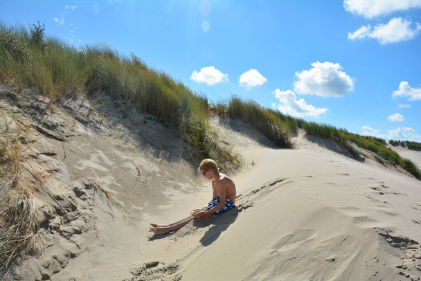 Poika istuu hiekkadyyneillä Pohjanmeren rannalla Alankomaissa kesällä - Valokuva, kuva