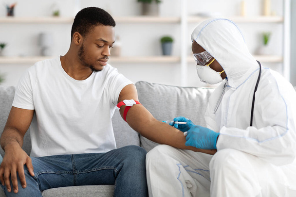 infermiera afro-americana che controlla il sangue dell'uomo alla ricerca di antigeni COVID-19 - Foto, immagini