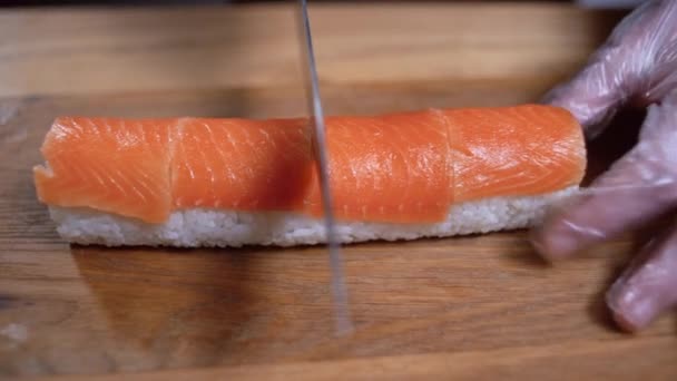 Le mani maschili tagliano il rotolo di sushi di tonno in metà su un tagliere. Tagliare i rotoli di sushi. - Filmati, video