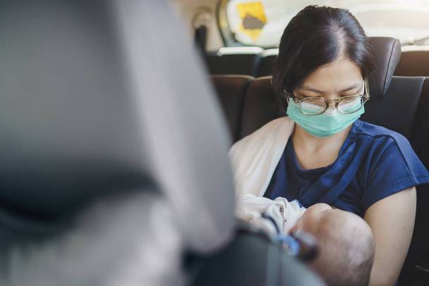 Asiática joven madre usando protección mascarilla celebración adorable bebé recién nacido niño mientras está sentado en el coche. Joven mamá amamantando a su hijo. - Foto, Imagen