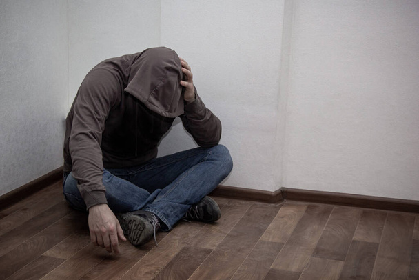 drogadicto joven y desesperado usando capucha y sentado solo en la esquina. concepto de tristeza, depresión y problemas de vida - Foto, imagen