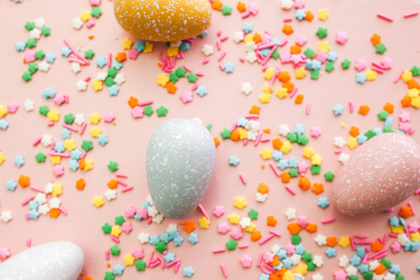 Huevos blancos, grises y amarillos sobre fondo rosa con salpicaduras de colores. Fondo de vacaciones de Pascua. - Foto, imagen