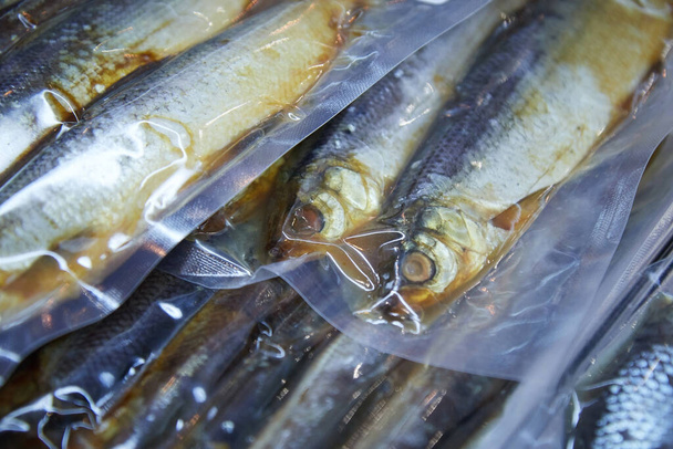 Balık ambalajının vitrinindeki füme ve kurutulmuş balıklarla dolu vakum ambalajı geçmişi bulanıklaştırdı. - Fotoğraf, Görsel