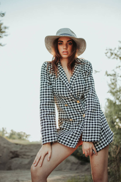 A portrait of a confident brunette woman wearing a coat with a houndstooth pattern and a fedora hat outdoors - Foto, immagini