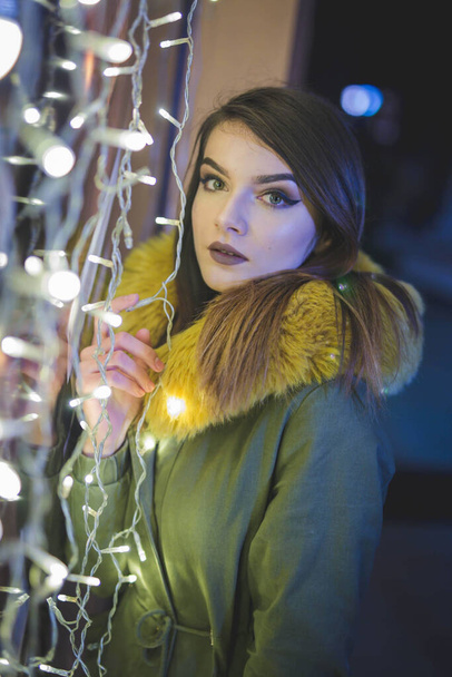 An attractive Bosnian Caucasian woman wearing a winter coat standing beside Christmas lights - Foto, Imagem