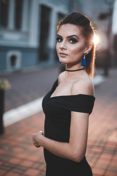 A vertical shot of an attractive young female in an elegant black dress posing in the street at night - 写真・画像