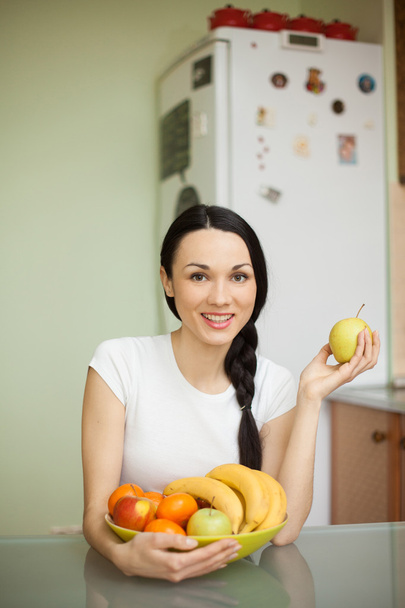 brunette girl holding fruits sitting in the kitchen  - Photo, image