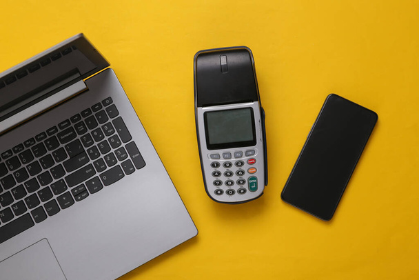 Terminal de pago con smartphone y portátil sobre fondo amarillo. Pago por compras. Compras en línea. Vista superior - Foto, Imagen