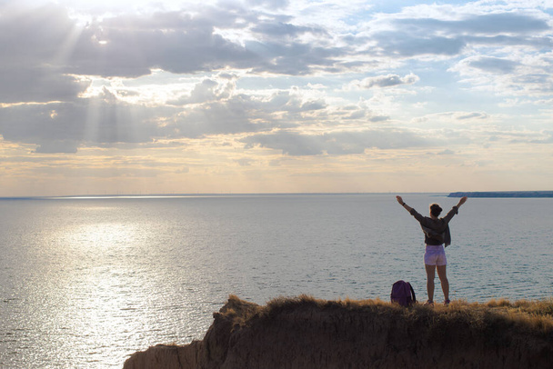 Widok z tyłu szczęśliwej kobiety na szczycie góry z otwartymi ramionami podnoszące świętowanie, turysta stojący na skale podczas zachodu słońca i patrząc na morze. Silna i wolna koncepcja stylu życia. Korzystanie z podróży przygodowych - Zdjęcie, obraz