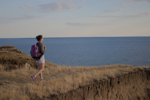 Jonge vrouw reiziger met rugzak wandelen het pad op bergtop, wandelen naar klif aan zee bij zonsondergang, genieten van het uitzicht op het natuurlandschap. Zachte filter.Wanderlust avontuur lifestyle concept - Foto, afbeelding