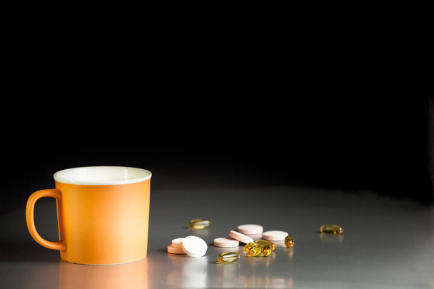 Tazza di ceramica arancione su un tavolo grigio su uno sfondo nero con capsule omega-3 e compresse effervescenti con vitamine. Integratori alimentari, vitamine, Omega-3. Assistenza sanitaria, supporto immunitario. - Foto, immagini