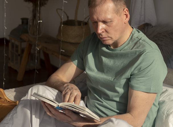 Middle-aged man reading book in cozy home, daylight. - Fotografie, Obrázek