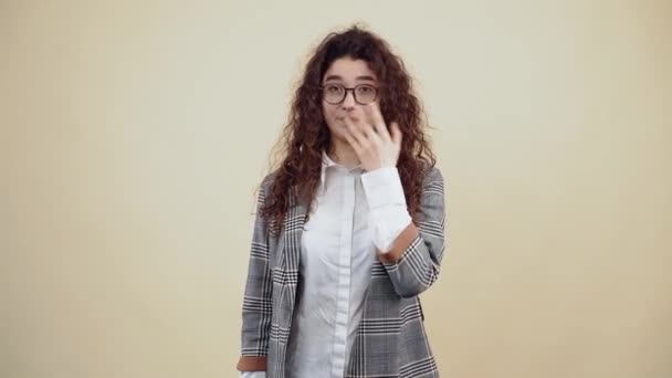 The young woman with curly sleepy hair, helmet and has a state of drowsiness. Young hipster in gray jacket and white shirt, with glasses posing isolated on beige background in the studio. - Footage, Video