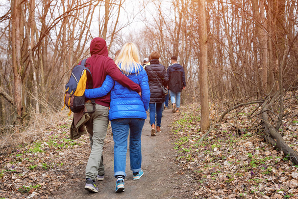 Grupa przyjaciół spacerujących z plecakami w wiosennym lesie od tyłu. Turyści wędrujący po lesie. Przygoda, podróże, turystyka, aktywny wypoczynek, wędrówka i ludzie koncepcja przyjaźni - Zdjęcie, obraz