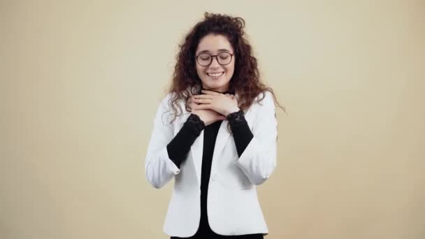 Happy and excited young woman with curly hair, she smiles while holding her hands to her chest and turns. Young hipster in gray jacket and white shirt, - Footage, Video