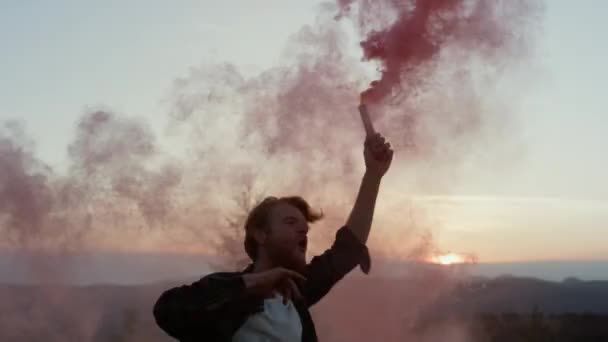 Guy tanzt in den Bergen bei Sonnenuntergang. Aufgeregter Typ mit aktiver Rauchgranate  - Filmmaterial, Video