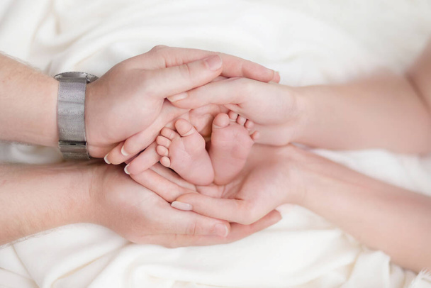 Parents hands hold in their hands the legs of their child on a white background, parental love and tenderness, the life of the child in the hands of his parents - Foto, imagen
