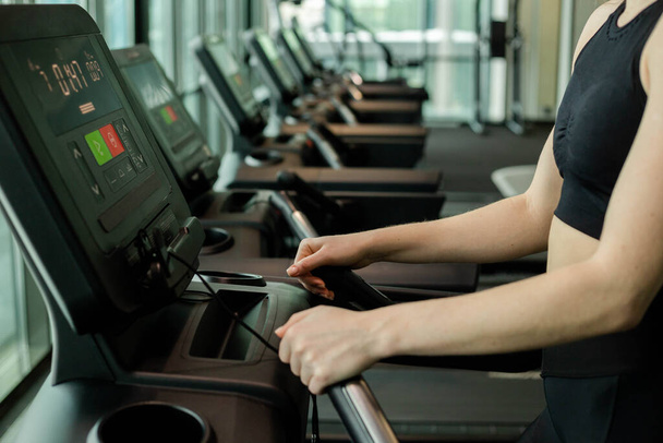 The athletic woman dressed in a black sportswear running on the treadmill in the modern gym. Fitness club concept. - Photo, Image