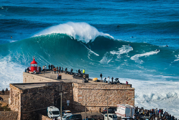 ポルトガルのナザレにあるサンミゲル・アルカンジョ灯台の近くで巨大な波に乗ってください。ナザレは世界最大の波を持つことで知られています. - 写真・画像
