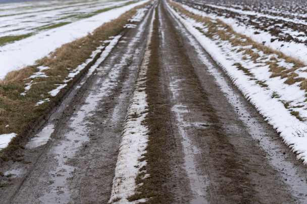 Route des champs de boue traversant les champs enneigés à la fin de l'hiver - Photo, image