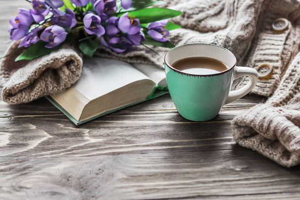  Ранкова кава. Чашка кави на дерев'яному столі, відкрита книга і теплий светр на тлі букета весняних квітів. Концепція натюрморту. Затишний ранок
. - Фото, зображення