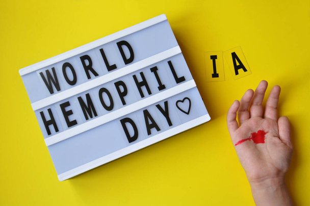 L'inscription Journée mondiale de l'hémophilie. Est célébrée chaque année le 17 avril. L'hémophilie se produit en raison de mutations génétiques sur le chromosome X et est héréditaire. Il se manifeste par une violation de la coagulation du sang. Main d'enfant avec coeur rouge - Photo, image