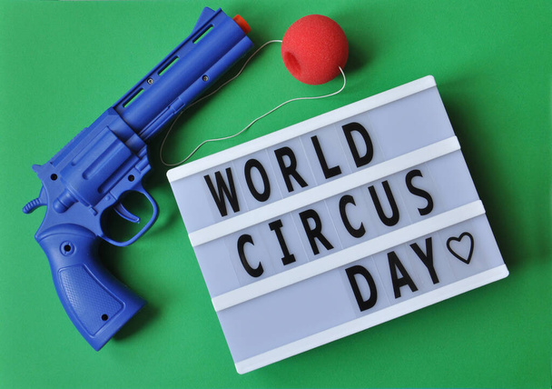 Nápis Mezinárodní den cirkusu se slaví v roce 2021, padá 17. dubna. Pozadí barevný klaun zbraň a nos. Pojem dětství a štěstí. - Fotografie, Obrázek