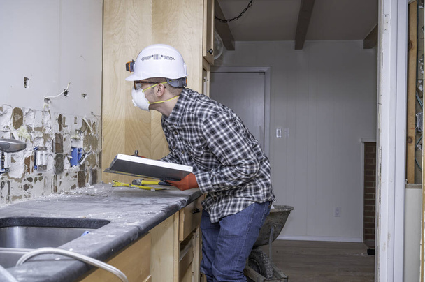 Electrician inspecting electrical outlet inside kitchen of a home remodel. - Photo, Image