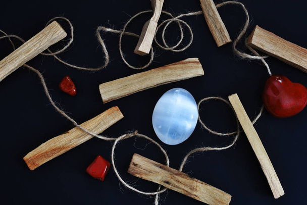 Une image de vue de dessus de bâtons de tache de bois sacré avec du sélénite et des cristaux de jaspe rouge sur un fond noir.  - Photo, image