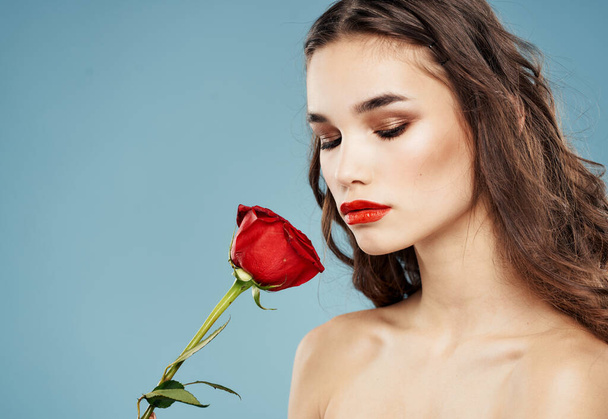 女性は青い背景に赤い花を手に持っていて、顔に化粧をしています - 写真・画像