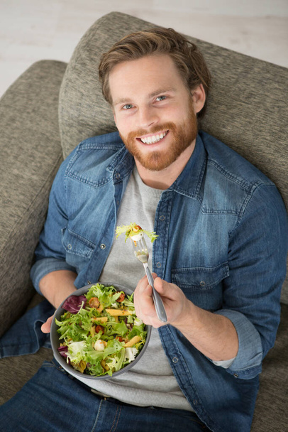 man laid on the sofa eating a salad - Фото, зображення