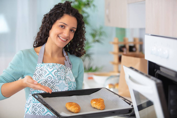 cheerful woman taking delicious crispy croissants from oven - Foto, Imagem