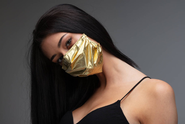 Preiserhöhung der Gesichtsmasken und Knappheit in COVID-19-mal Konzept als schöne junge Frau mit einer Gesichtsmaske aus Gold, weil sie es sich leisten kann, auch wenn sie zu einem extrem seltenen Gut geworden sind - Foto, Bild