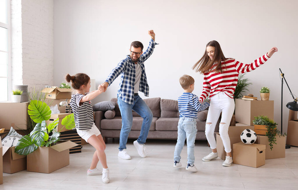 Familia de cuerpo completo: madre y padre tomados de la mano y bailando con la hija y el hijo cerca del sofá y cajas de cartón con pertenencias en el nuevo  - Foto, imagen