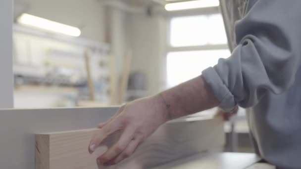 Nahaufnahme eines jungen kaukasischen Tischlers in Schutzbrille, der bei seiner Arbeit in der Möbelfabrik raue Kanten von Naturholzplatten auf der Tischler-Drehbank schneidet - Filmmaterial, Video