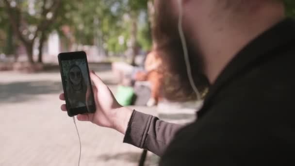 携帯電話を持っている髭の男の肩のショットの上に追跡とビデオ通話女性屋外 - 映像、動画