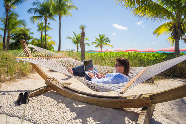 Giovane uomo che lavora su laptop in amaca sulla spiaggia tropicale
 - Foto, immagini