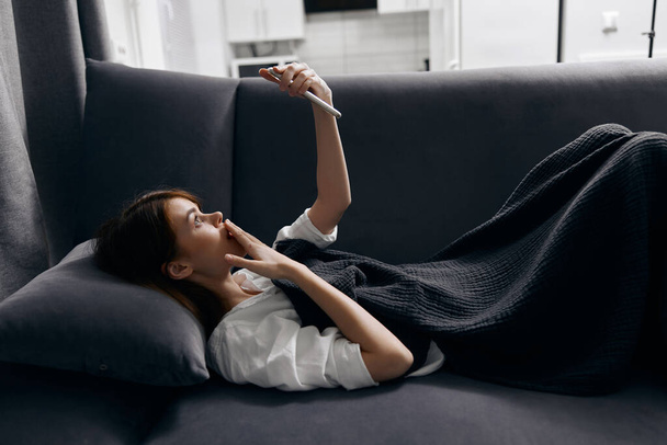 kobieta leży na poduszce z telefonem komórkowym w ręku i szarym wnętrzem sofy - Zdjęcie, obraz