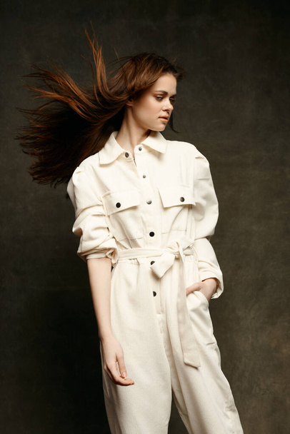 beautiful brunette in a light jumpsuit on a dark background keep her hands in her pocket - Fotografie, Obrázek