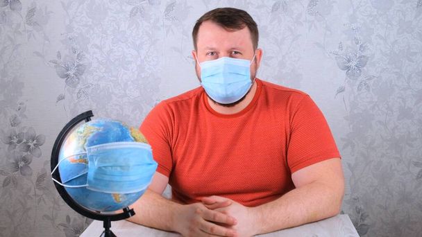 O macho está a olhar para o globo com uma máscara protectora e uma vacina pandémica. Conceito de tratamento do vírus Corona, injeção, ensaios clínicos durante uma pandemia. Conceito de viagem durante uma pandemia - Foto, Imagem