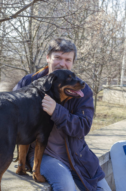 Συναισθηματικό πορτραίτο ενός θλιμμένου άντρα που του λείπει το κατοικίδιό του. Η πολυαναμενόμενη συνάντηση του σκύλου και του ιδιοκτήτη μετά από ένα μεγάλο χωρισμό. Σκυλίσια ράτσα Rottweiler. Εξωτερικές πόρτες. - Φωτογραφία, εικόνα
