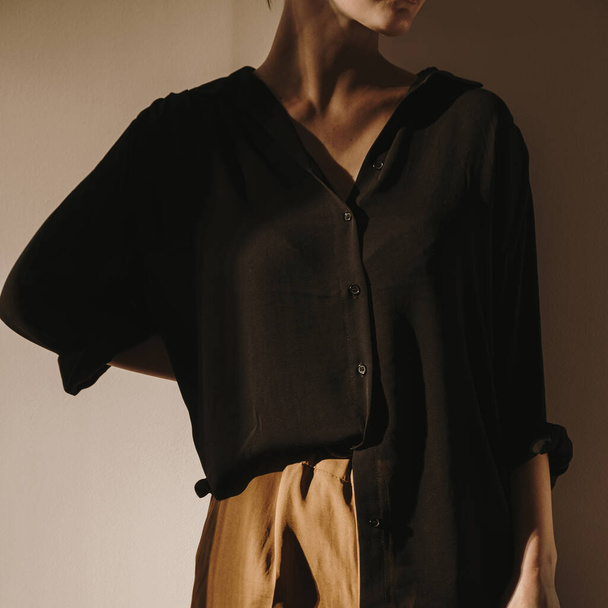 Молода красива жінка в чорній сорочці і коричневі штани залишаються на стіні. Стан сонячних променів на стіні. Мінімальна естетична краса, концепція моди для журналу, блогу, соціальних медіа
. - Фото, зображення
