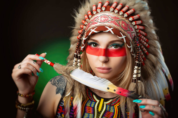portret van een vrouw naar het beeld van een Amerikaanse indiaan in een kakkerlak hoofdtooi met een pen in haar handen - Foto, afbeelding