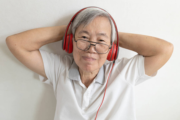 Азійська старша жінка в навушниках, яка слухає музику онлайн на мобільному телефоні, літні люди у червоних навушниках, відпочивають у вільний час, насолоджуються музикою, залишаються вдома, технологія, спосіб життя. - Фото, зображення