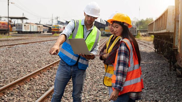 Succesvolle spoorweglogistiek specialisten of treiningenieurs met helmen en veiligheidsvesten voeren inspecties uit en voldoen aan een werkplan voor het beheer van een goederentrein op het spoor. - Foto, afbeelding