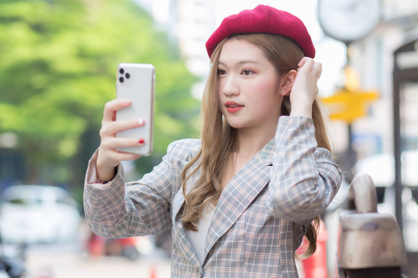 Asian woman in bronze hair takes selfie photo by smartphone on street as background. - Photo, Image