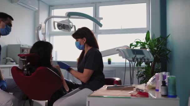 Οι γιατροί οδοντίατροι γυναίκα και ο άνθρωπος με ιατρικές μάσκες εξυπηρετούν τον ασθενή στην οδοντιατρική κλινική - Πλάνα, βίντεο